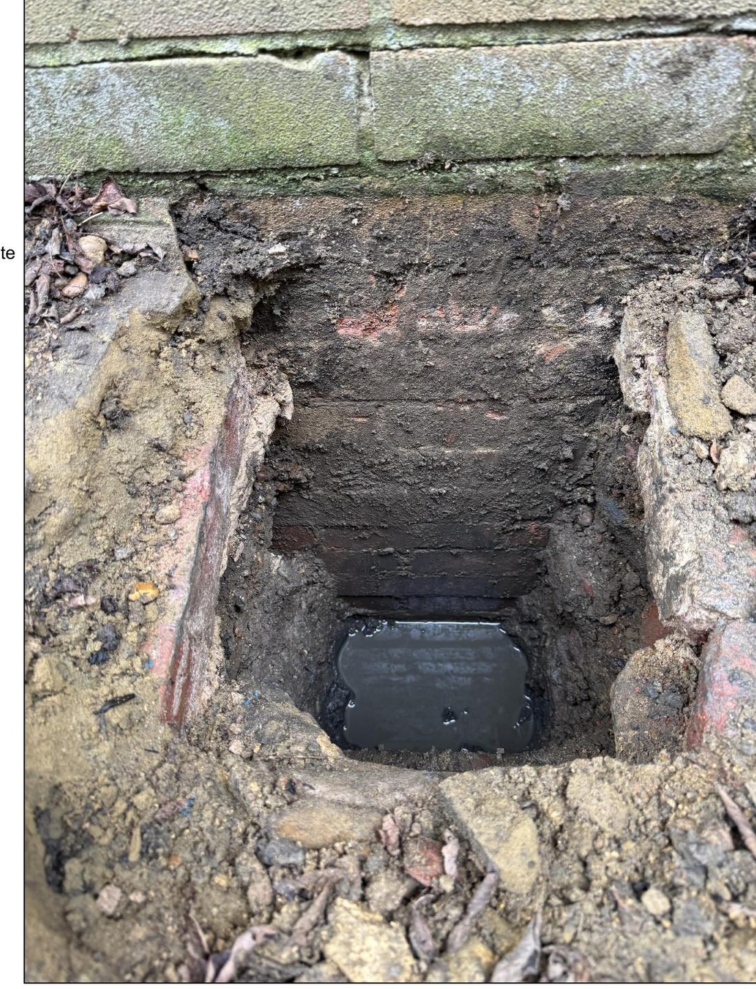 Trial pit beside the garage wall exposing the existing brick footing and concrete